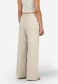 Beige széles szárú nadrág puha anyagból, elasztikus derékpánttal és oldalzsebekkel, sima tapintású és minimalista varrási részletekkel.