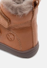 Botte en cuir marron avec une doublure en fourrure grise douce. Présente un accent en étoile et des coutures contrastées le long des seams. Semelle en caoutchouc robuste.