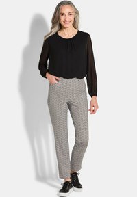 Zwarte blouse met lange mouwen en gathered halslijn, gecombineerd met een patroon van slim-fit broek in wit, zwart en beige. Zwarte sneakers accentueren de outfit.