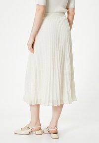Gonna midi plissettata di colore crema con piccole pois nere. Tessuto morbido, cintura elastica, abbinata a scarpe con tacco a blocco beige.