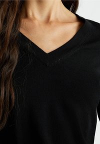 Schwarzer V-Ausschnitt-Pullover mit strukturiertem Kragen, aus glattem Strickstoff mit figurbetonter Passform, der ein einfaches, klassisches Design hervorhebt.