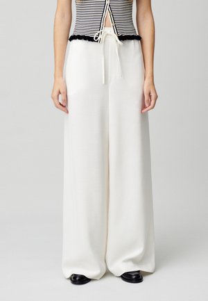 Pantalon large blanc avec une texture douce et une taille à cordon. Associé à un haut ajusté noir et blanc à rayures avec un ourlet froncé.