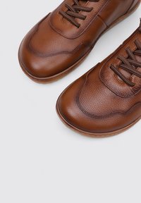 Zapatos de piel marrón con cordones que presentan una superficie texturizada, puntera redonda y costuras contrastantes en la parte superior y la suela de goma.