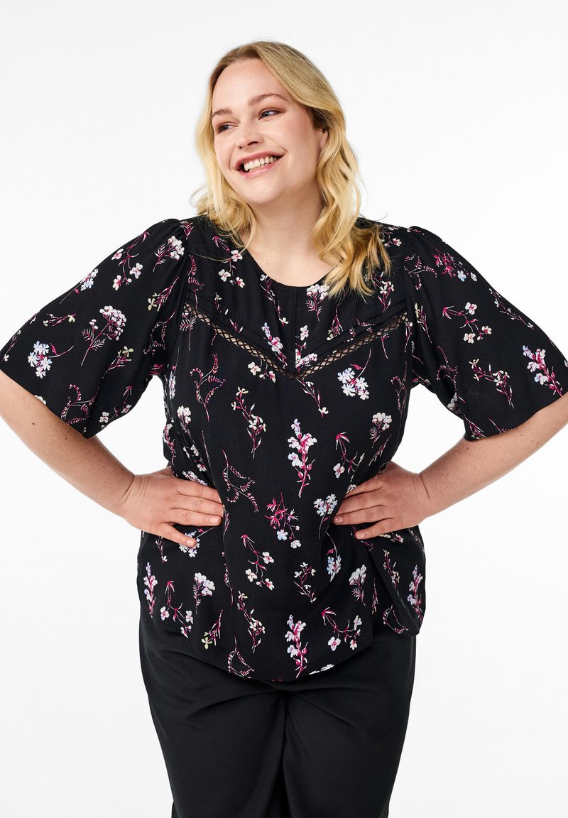 Blusa nera a fiori con maniche corte a palloncino, caratterizzata da un motivo floreale nei colori pastello e dettagli in pizzo lungo il collo.