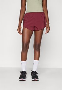 Mörkröda atletiska shorts med elastisk midja, med en diskret logotyp på sidan. Matchas med svarta sneakers och vita ankelsockor.