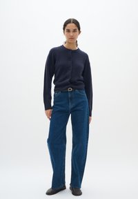 Marinblå kofta med rund hals och fem knappar, kombinerad med högmidjade, vida blå jeans och svarta ankelskor.