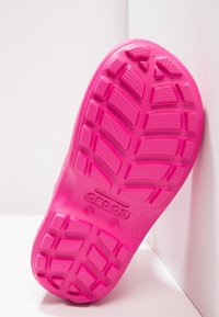 Suela de goma rosa de Crocs con un patrón de banda de rodadura que presenta hexágonos y rectángulos elevados para mayor agarre, etiquetada con la talla y "hecho en Vietnam".