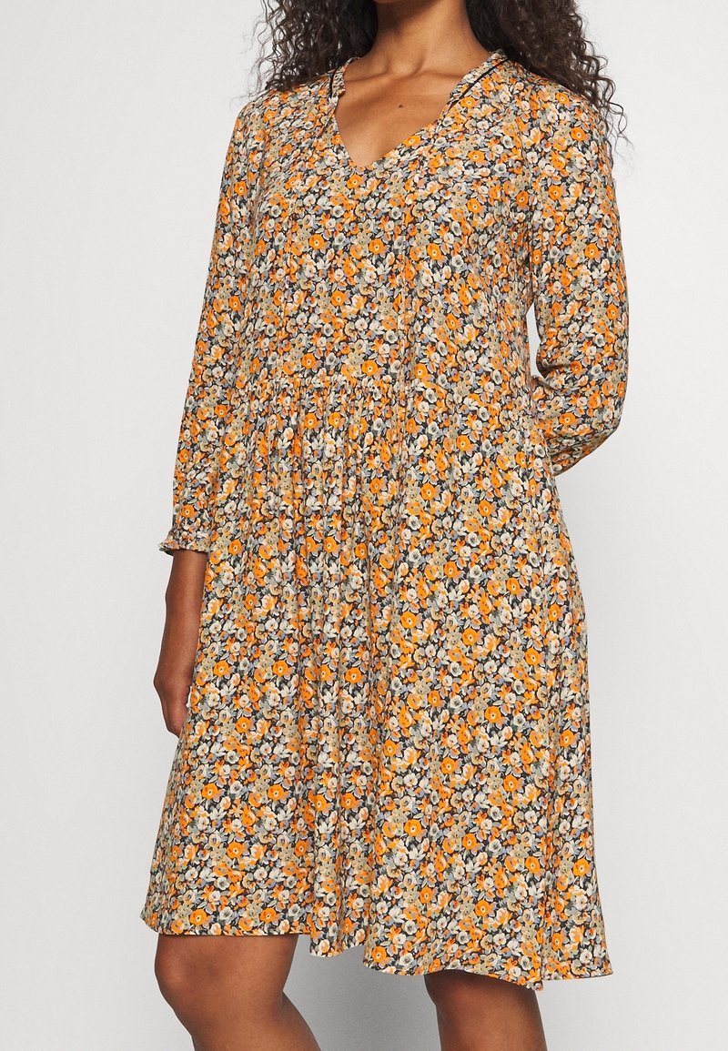 Blomstret kjole med lange ærmer, V-halsudskæring og indsnævret talje. Har et mønster af orange blomster på en mørk baggrund. Letvægtsstof.