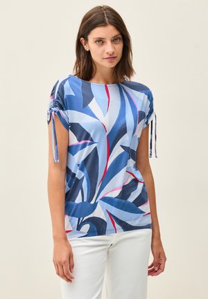 Haut bleu à manches courtes avec un motif de feuilles abstrait dans des nuances de bleu, marine et rose ; présente des détails de cordon de serrage sur les manches.