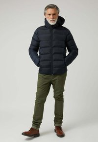 Chaqueta de abrigo azul marino con secciones acolchadas horizontales, cremallera frontal y capucha, combinada con pantalones verdes oliva y botas marrones con cordones.