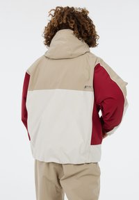Kleurgeblokte jas met beige, witte en bordeauxpaneel. Gemaakt van een glad, lichtgewicht materiaal met een capuchon en logo-detail.