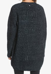 Mørk strikket cardigan med løs pasform, der har et struktureret mønster og en lille knapdetalje på ryggen, velegnet til lag-på-lag stil.