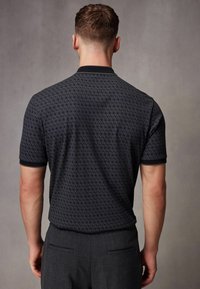 Polo cu mânecă scurtă de culoare bleumarin închis, cu un model texturat, repetitiv. Dispune de guler și manșete negre. Croială ajustată cu un finisaj neted.