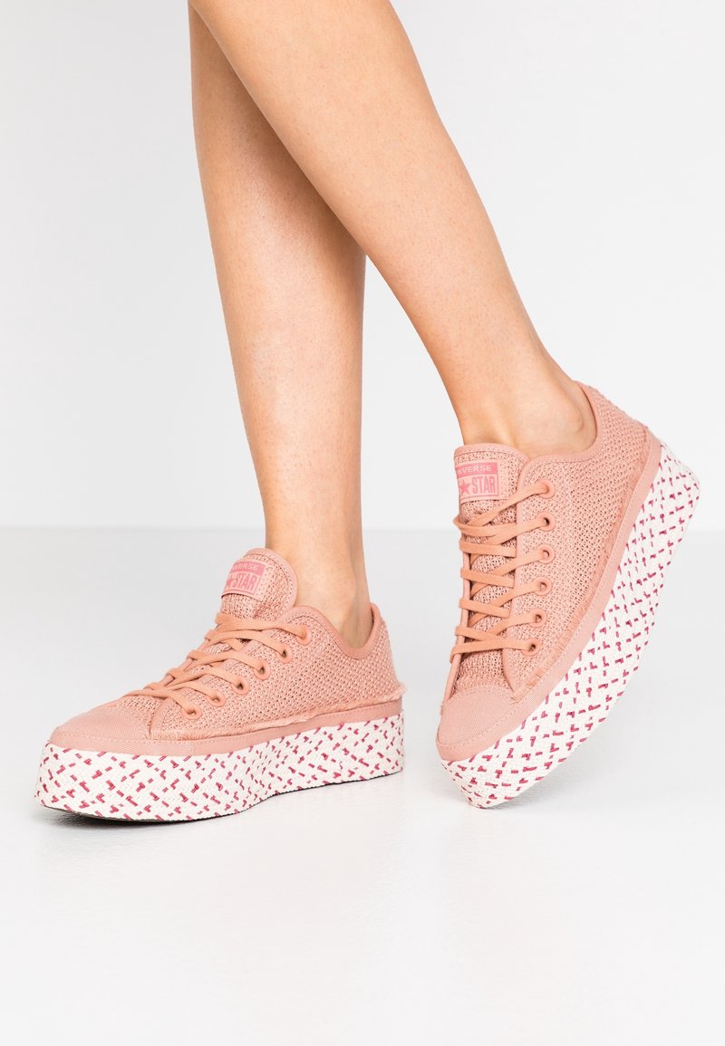 Różowe siateczkowe sneakersy na białej teksturowanej platformie z czerwonymi geometrycznymi wzorami, okrągłymi sznurowadłami i oznaczeniem marki na języku.