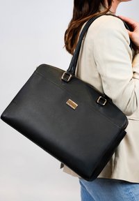 Zwarte leren tote bag met een gestructureerde vorm, gouden hardware accenten en een ritssluiting. Bevat dubbele schouderbanden voor het dragen.