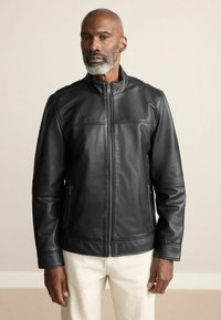 Schwarze Lederjacke mit Stehkragen, frontaler Reißverschluss und Seitentaschen. Glatte Textur mit subtilen Nahtakzenten.