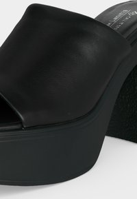 Sandale plateforme en cuir noir à bout ouvert avec talon épais et bride supérieure lisse sur fond blanc.