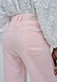 Pantalones de mezclilla rosa claro con bolsillos traseros y una etiqueta que dice "Salsa Jeans". Combinados con una blusa blanca bordada.