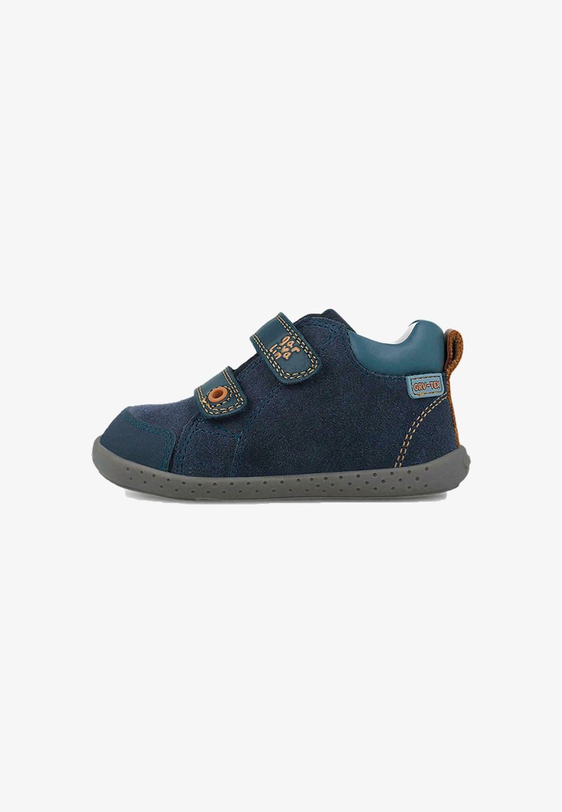Zapato de ante azul marino con dos correas de Velcro, acentos en verde azulado, suela de goma gris y detalles en cuero marrón en el talón.