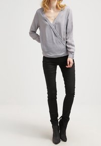 Blusa avvolgente grigia chiara con maniche lunghe e scollatura a V profonda, abbinata a jeans skinny neri e stivaletti alla caviglia. Tessuto morbido, design casual.