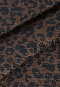 Materijal s leopard uzorkom ima smeđu pozadinu s crnim mrljama. Tkanina ima teksturirani, rebrasti završetak s mrljama različitih oblika.