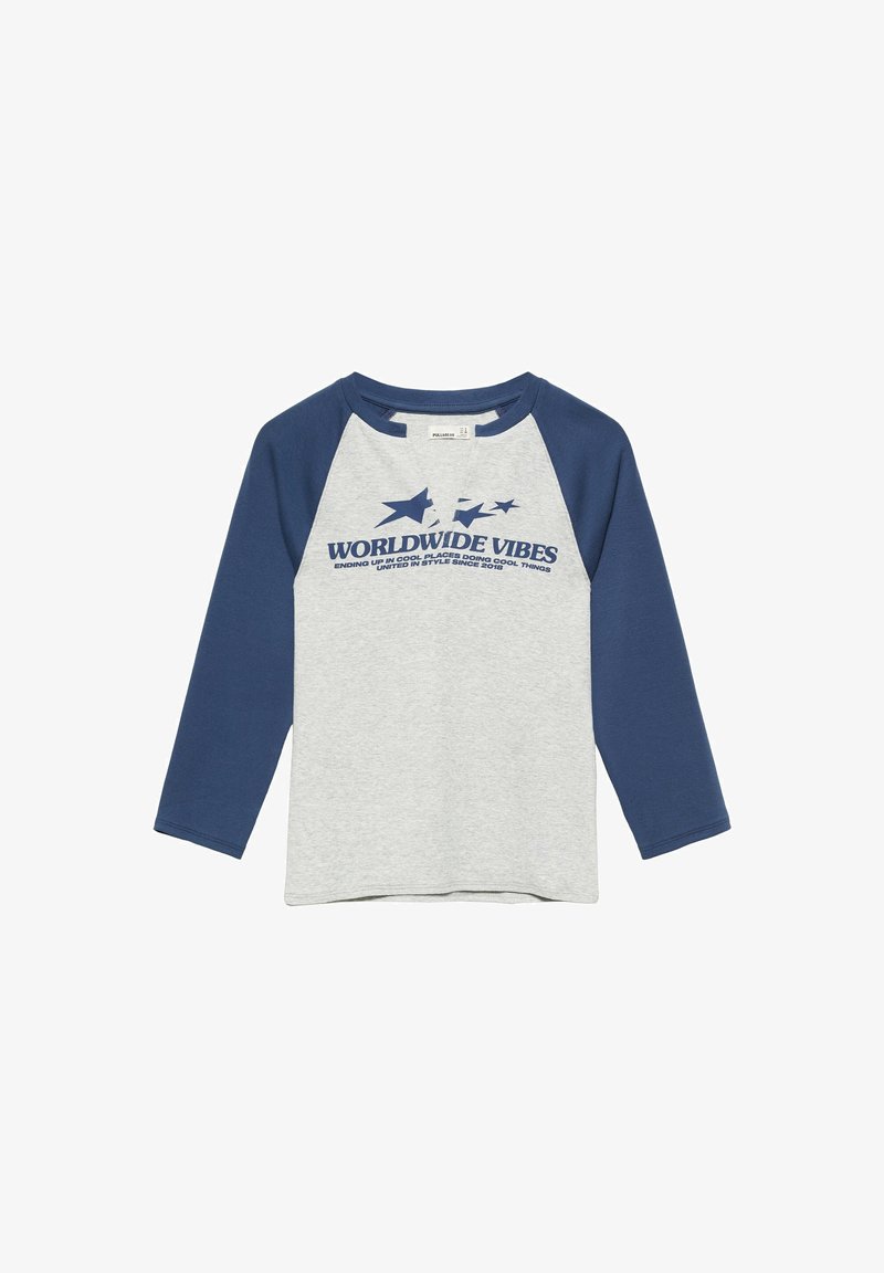 T-shirt raglan manches longues avec manches bleu marine et corps gris clair, avec le texte "Worldwide Vibes" et des graphismes d'étoiles sur la poitrine.