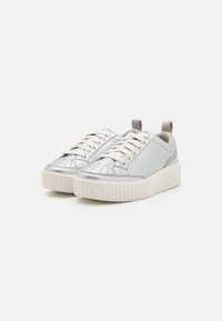 Silver sneakers with a textured metallic finish, featuring white laces, a padded collar, and a thick, ridged white sole.
