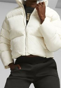 Weißer Puffer-Jacke mit Reißverschluss vorne, hohem Kragen und gestepptem Material, kombiniert mit schwarzen gerippten Hosen mit Seitentaschen.
