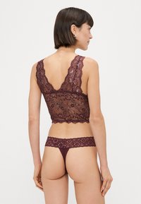 Mežģīņu bralete un atbilstoši stringi dziļi burgundijas krāsā. Iezīmējas ar sarežģītajām ziedu rakstiem, viļņotām malām un caurspīdīgu tekstūru.