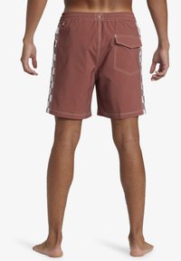 Men's swim shorts in rust color with white checkered side panels, elastic waistband, back pocket, and contrasting stitching details.