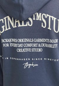 Sudadera azul marina con texto impreso en blanco que detalla el nombre de la marca y el eslogan, con una textura suave y capucha con cordón.