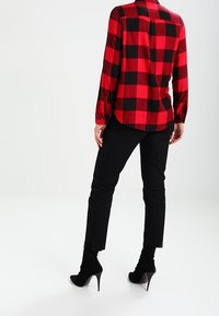 Persona che indossa una camicia a maniche lunghe a scacchi rossi e neri, pantaloni neri aderenti e stivaletti neri con tacco alto in posizione con la schiena rivolta.