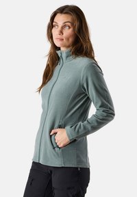 Fleece zip-up jacket in light teal, featuring a high collar, two side pockets, and a smooth texture. No visible logos or patterns.