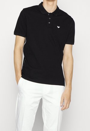 Black polo shirt made of cotton, featuring a classic collar, three-button placket, and small logo on the chest. Short sleeves.