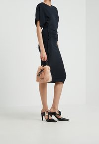 Svart figurnära klänning med korta ärmar och sidofållningar; mjuk rosa fuskpälsväska; svarta spetsiga klackskor med cirkulära detaljer och utskärningar.