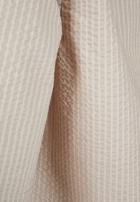 Cremefarbener Waffelstoff mit strukturiertem quadratischem Muster, der in weichen Falten hängt.