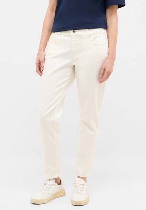 Cream colored slim-fit pants with a smooth texture, low-rise waist, and five-pocket design. Paired with white sneakers.