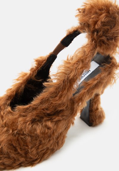 Καφέ χνουδωτό γόβα με ψηλό τακούνι τύπου slingback, με μαύρο τακούνι και λουράκι που φέρει λεπτομέρεια πομ-πομ και εμφανές εσωτερικό λογότυπο της μάρκας.