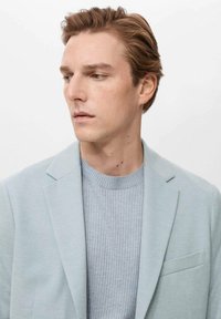 Light blue blazer over a gray ribbed sweater. The blazer features a notched collar and a single pocket. Smooth fabric texture.