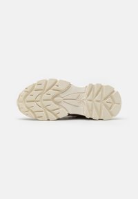 Suela de goma color blanco roto de una zapatilla con surcos profundos y patrones texturizados para un mejor agarre, presentada sobre un fondo blanco liso.