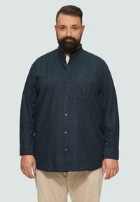 Dunkelblauses Langarmhemd mit Kragen, Brusttasche und strukturiertem Stoff. Kombiniert mit hellen Cordhose.