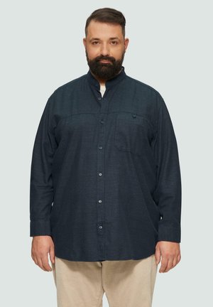 Chemise à manches longues bleu foncé avec col, poche avant et tissu texturé. Associée à un pantalon en velours côtelé de couleur claire.