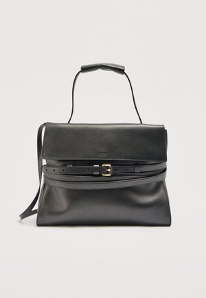 Sac à main en cuir noir avec une fermeture à rabat, une anse supérieure et une longue bandoulière réglable ornée d'une boucle dorée sur un fond uni.