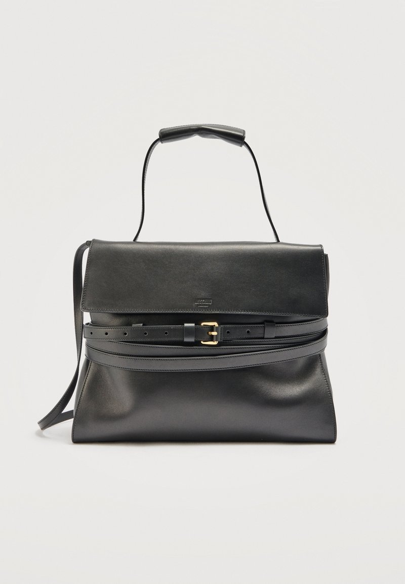 Sac à main en cuir noir avec une fermeture à rabat, une anse supérieure et une longue bandoulière réglable ornée d'une boucle dorée sur un fond uni.