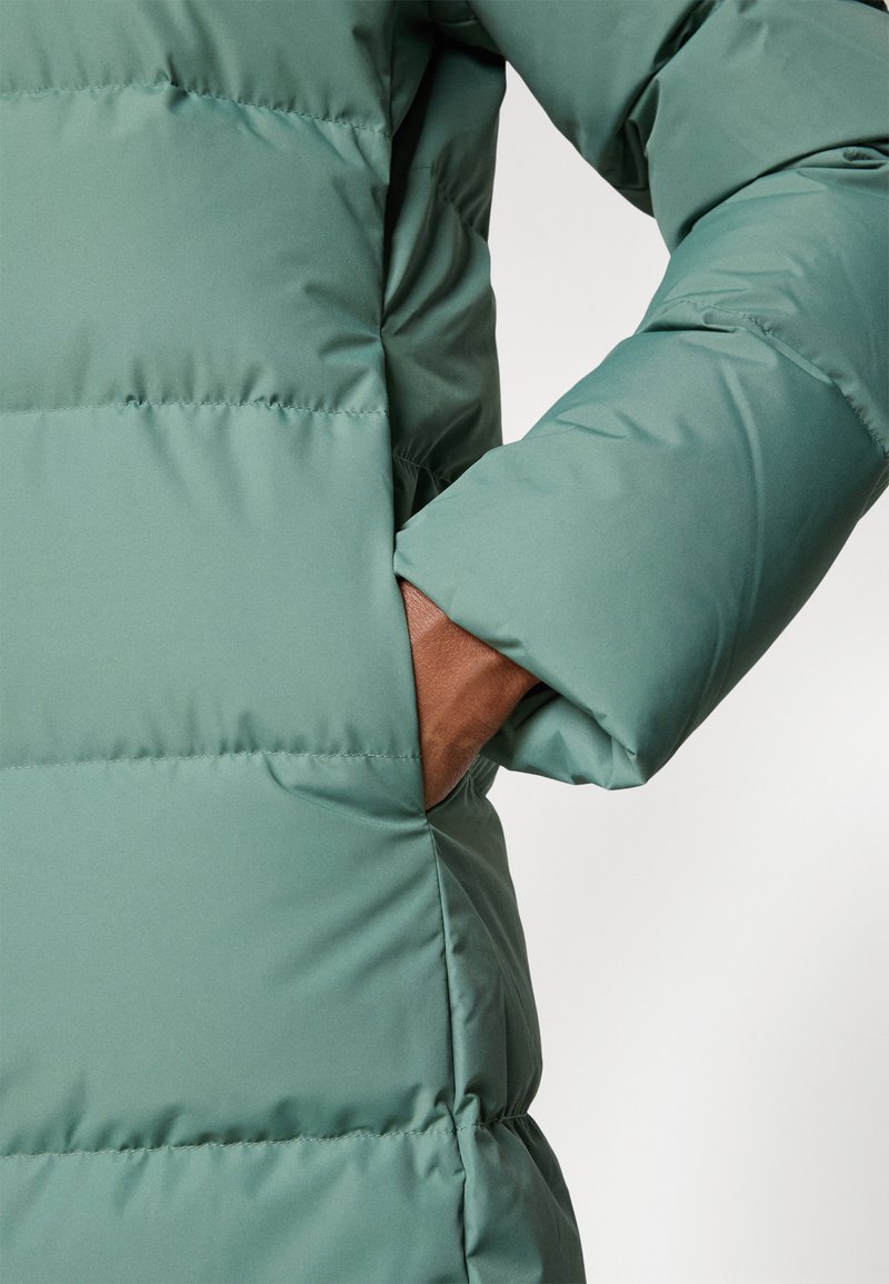 Grüne Pufferjacke mit glatter Textur, ausgestattet mit einer Seitentasche und einem eng anliegenden Ärmeldesign.