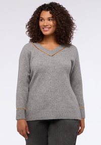 Suéter de punto gris con escote en V, que presenta acentos de cadena en tono dorado a lo largo del escote y los puños. Textura suave y corte relajado.