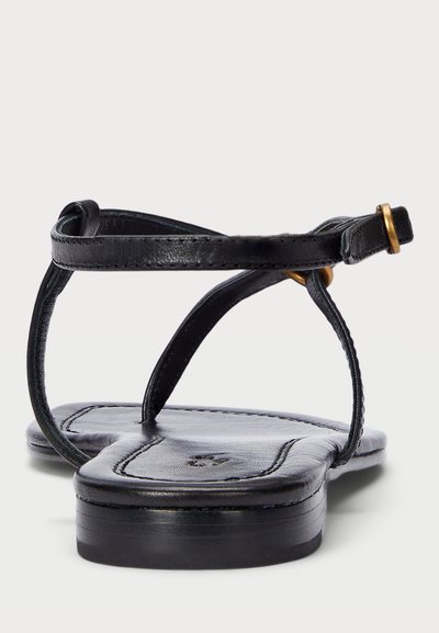 Μαύρες δερμάτινες σαγιονάρες με επίπεδη σόλα, που διαθέτουν μινιμαλιστικούς, λεπτούς ιμάντες και χρυσή λεπτομέρεια στον ιμάντα του αστραγάλου για ασφαλή εφαρμογή.