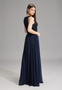 Navy Abendkleid mit einem Spitzenoberteil mit gewelltem Detail und einem fließenden Rock. Der Stoff ist glatt und leicht, ideal für formelle Anlässe.