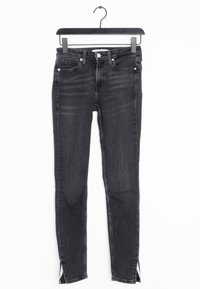 Jeans skinny de mezclilla negra con una cintura de media altura, que cuentan con aberturas laterales en el dobladillo y un estilo clásico de cinco bolsillos. Textura suave.