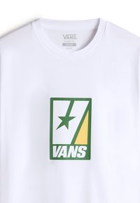 Bílá bavlněná tričko s zelenožlutou grafickou nálepkou se hvězdou a textem "VANS." Klasický střih s kulatým výstřihem.